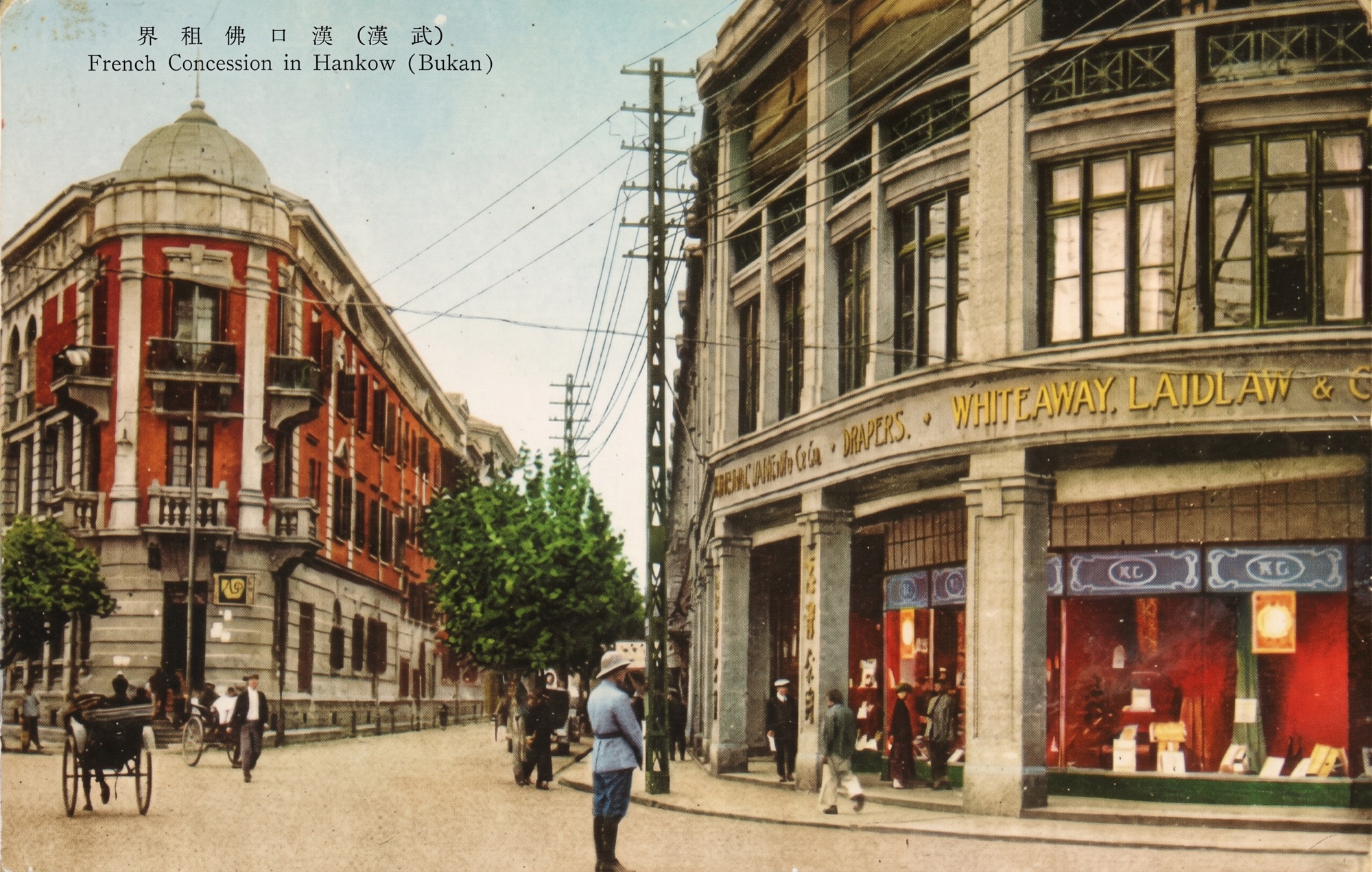 Postal antigua coloreada de la Concesión Francesa en Hankow: un edificio de ladrillo rojo con cúpula, los almacenes Whiteaway Laidlaw a la derecha y un policía con casco colonial en la calle
