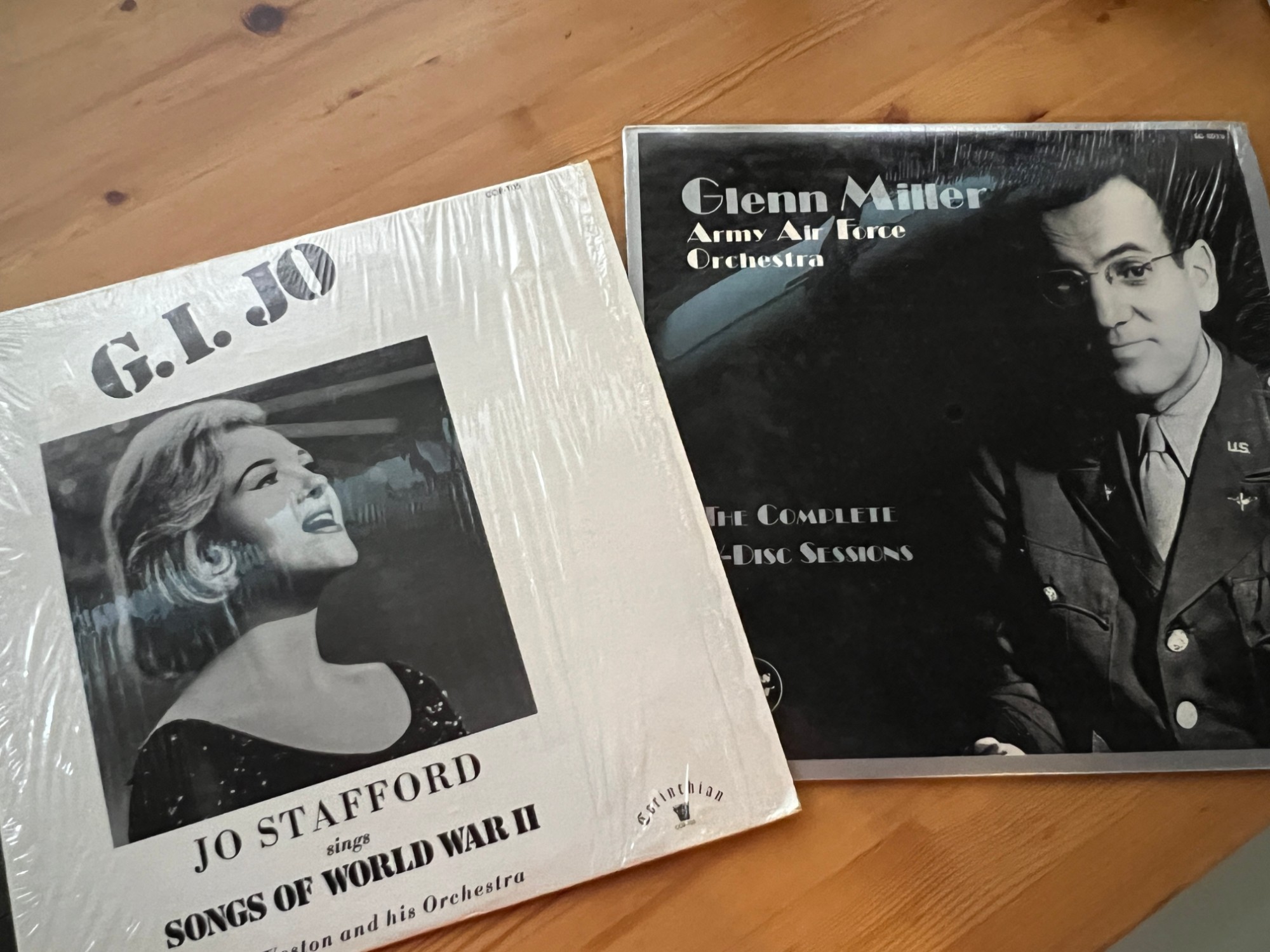 Two vinyl LPs on a wooden table: G.I. JO – Jo Stafford sings Songs of World War II (Corinthian Records), and Glenn Miller and the Army Air Force Orchestra – The Complete V-Disc Sessions